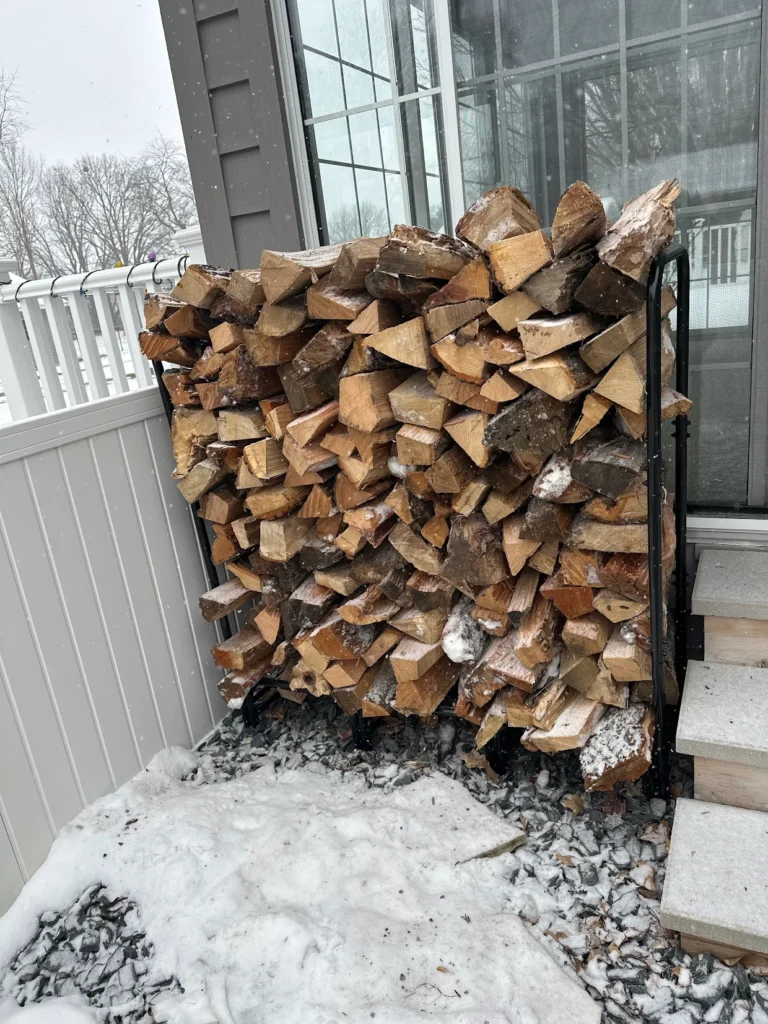 A photograph of firewood stacked on a rack in the snow.